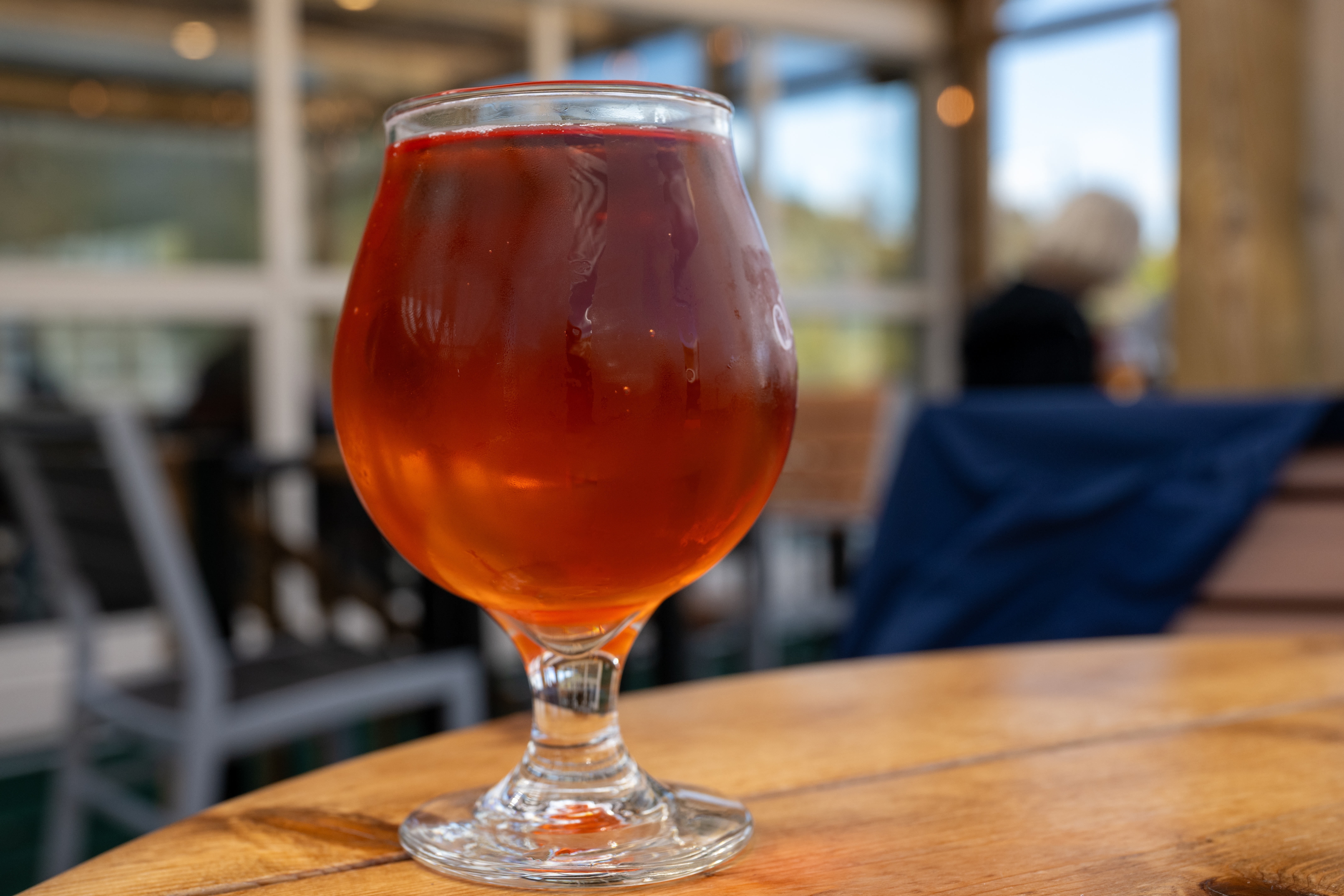 Et stilket glas fyldt med rød frugt ale craft øl på et træbord på en bryggeribar
