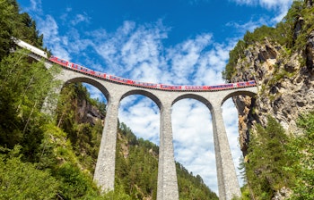 Rød Gletsjer-ekspres krydser den historiske Landwasser Viadukt i de schweiziske alper på togrejsen gennem bjerglandskabet