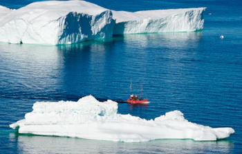 Rødt skib sejler mellem kæmpestore isbjerge ved Sermermiut nær Ilulissat i Grønland