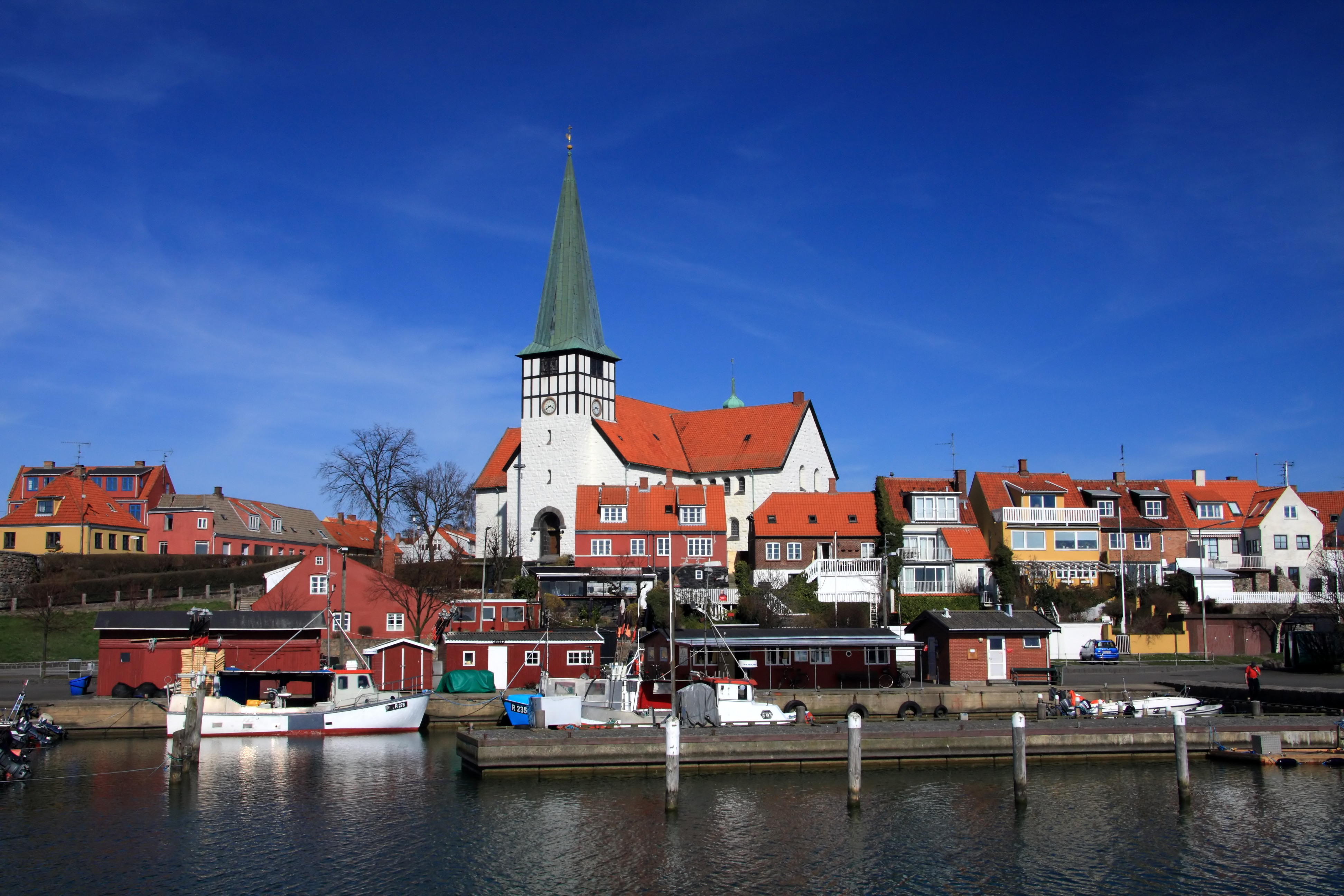 Rønne havn med farverige fiskerbåde og den karakteristiske kirke med grøn spir over de røde tage på Bornholm
