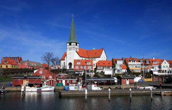 Rønne havn med farverige fiskerbåde og den karakteristiske kirke med grøn spir over de røde tage på Bornholm