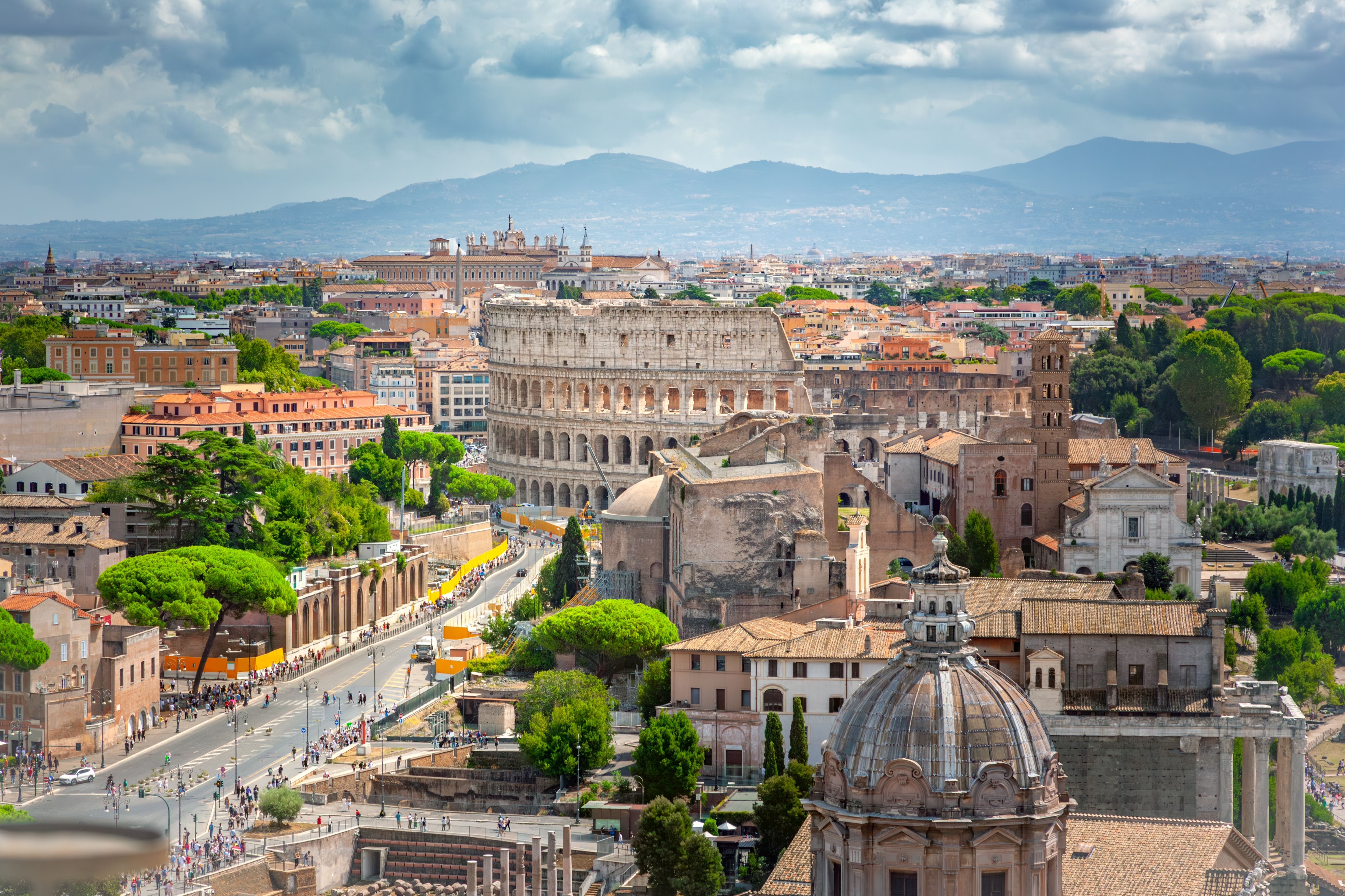 Betagende panoramaudsigt over Rom med det historiske Colosseum, antikke ruiner og bjergene i baggrunden set fra Palazzo Vittoriano