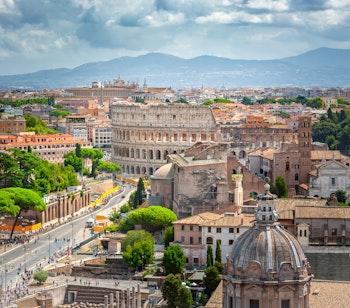 Betagende panoramaudsigt over Rom med det historiske Colosseum, antikke ruiner og bjergene i baggrunden set fra Palazzo Vittoriano
