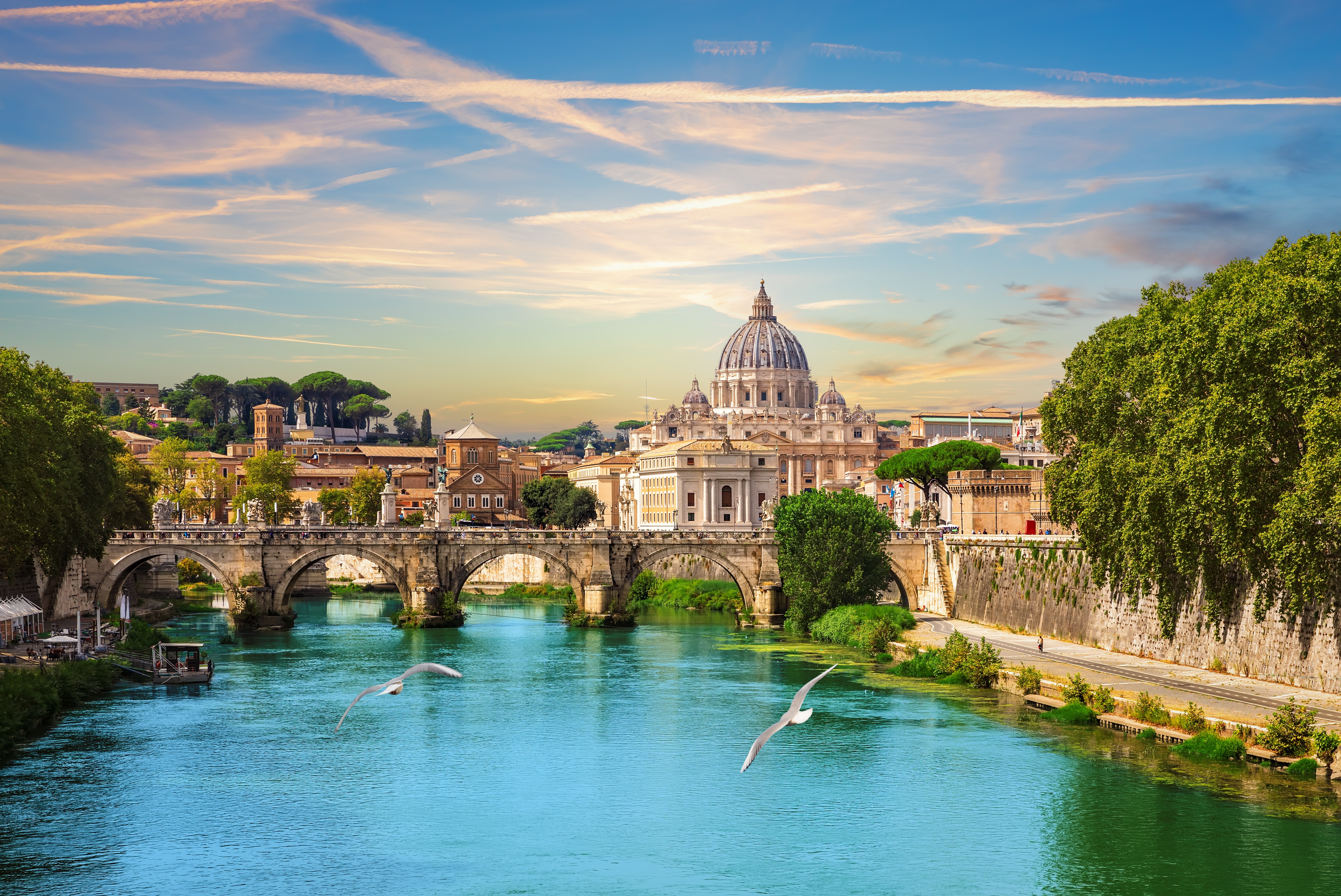 Smuk udsigt over Rom med Sankt Peters Basilika og Tiberen i solnedgang med Ponte Sant'Angelo i forgrunden