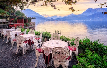 Hyggelig cafe med borde ved Comosøens bred i Italien med panoramaudsigt over Alperne under en farverig solnedgang