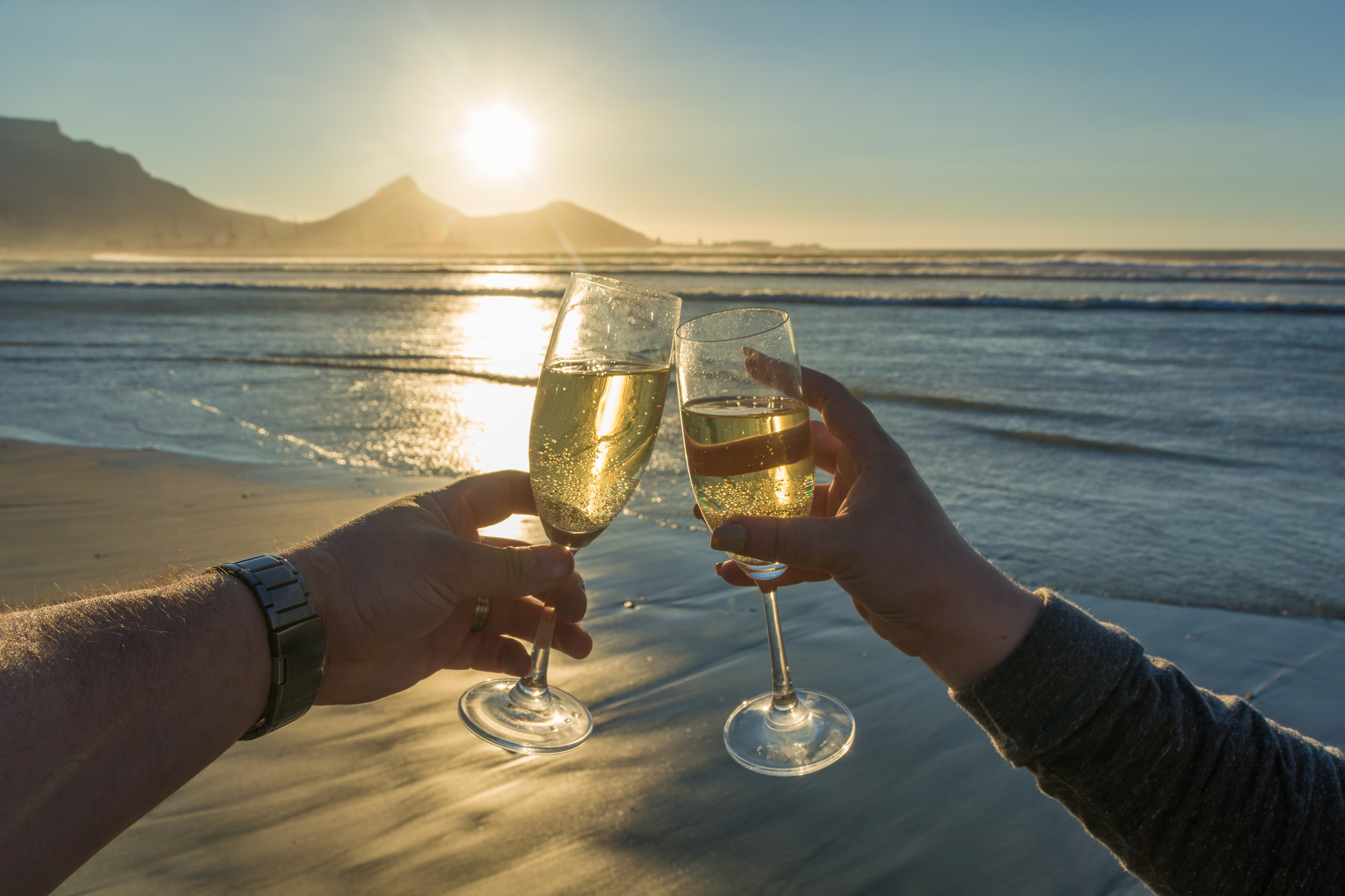 Romantisk champagne skål ved solnedgang på strand med bjerglandskab - luksus strandferie