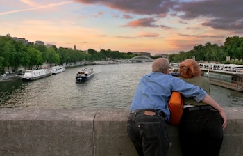 Ældre par nyder romantisk solnedgang over Seine-floden fra en bro i Paris med krydstogts-både