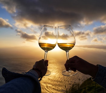 Romantisk par skåler med vinglas under gylden solnedgang over havet