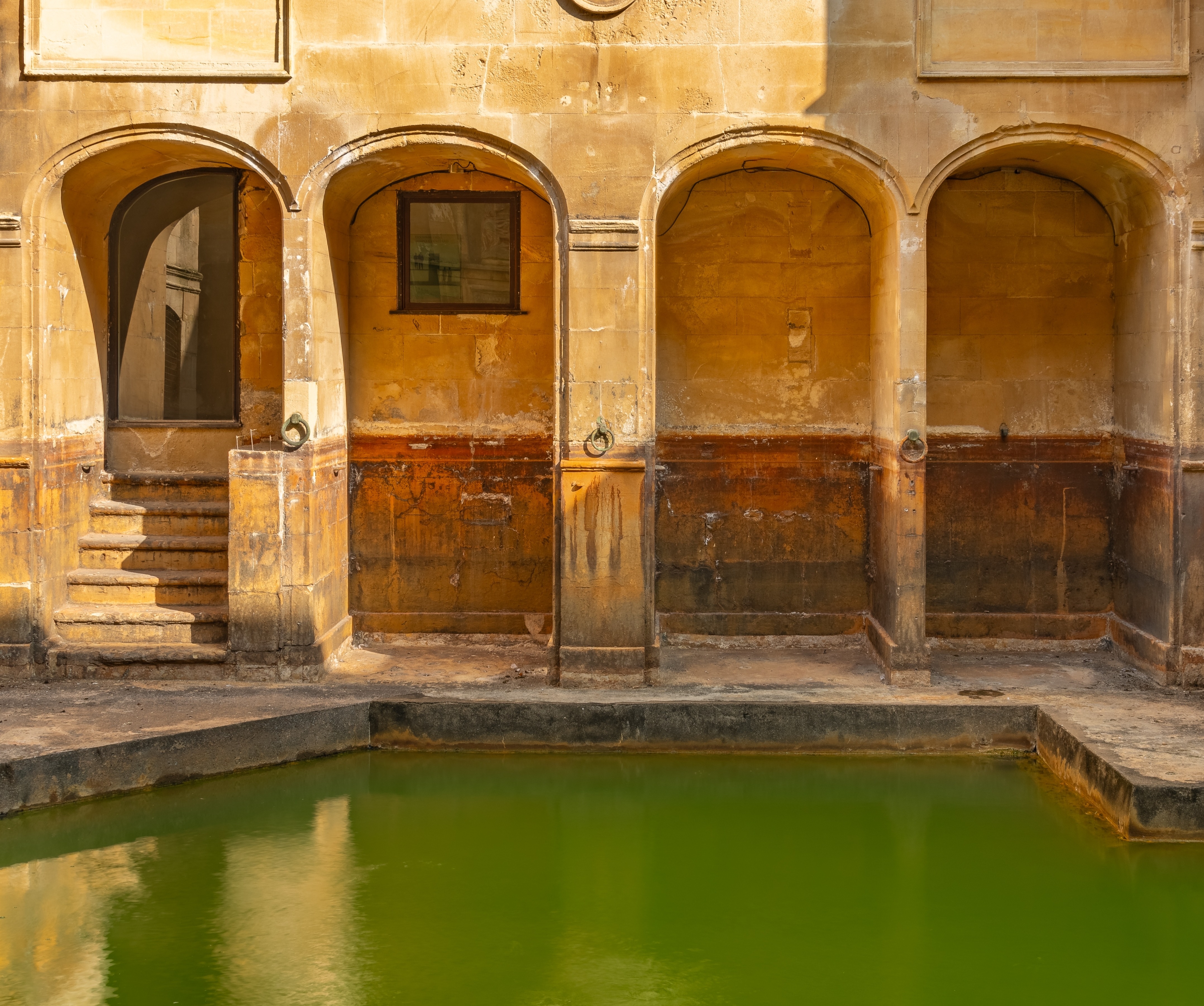 Antikke romerske bad med grønt termisk vand og historiske stenbuer i Bath England