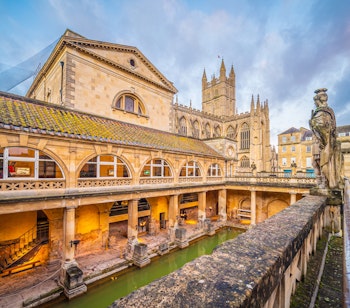 De historiske romerske bade i Bath, England, smukt oplyst i skumringen med det gyldne stenmurværk reflekteret i det termiske vand