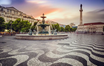 Rossio Torv i Lissabon ved solnedgang med historisk fontæne, bølgende brosten og Pedro IV-søjlen - perfekt til nytårsfejring i Portugals hovedstad