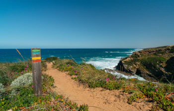 Farverig trailmarkering på Fishermans Trail langs Rota Vicentina i Portugal med dramatiske klippekyster og det blå Atlanterhav i baggrunden