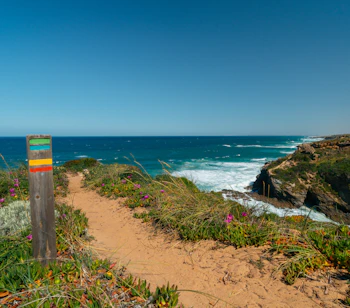 Farverig trailmarkering på Fishermans Trail langs Rota Vicentina i Portugal med dramatiske klippekyster og det blå Atlanterhav i baggrunden