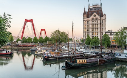 Historiske skibe i Rotterdams gamle havn Oude Haven med Willemsbrug-broen og moderne skyline, der spejler sig i vandet ved aftenlys om sommeren i Holland