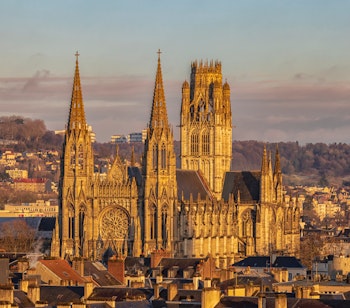 Majestætisk gotisk katedral i Rouen badet i gyldent solnedgangslys med karakteristiske spir og rosette-vindue over byens historiske centrum i Normandiet