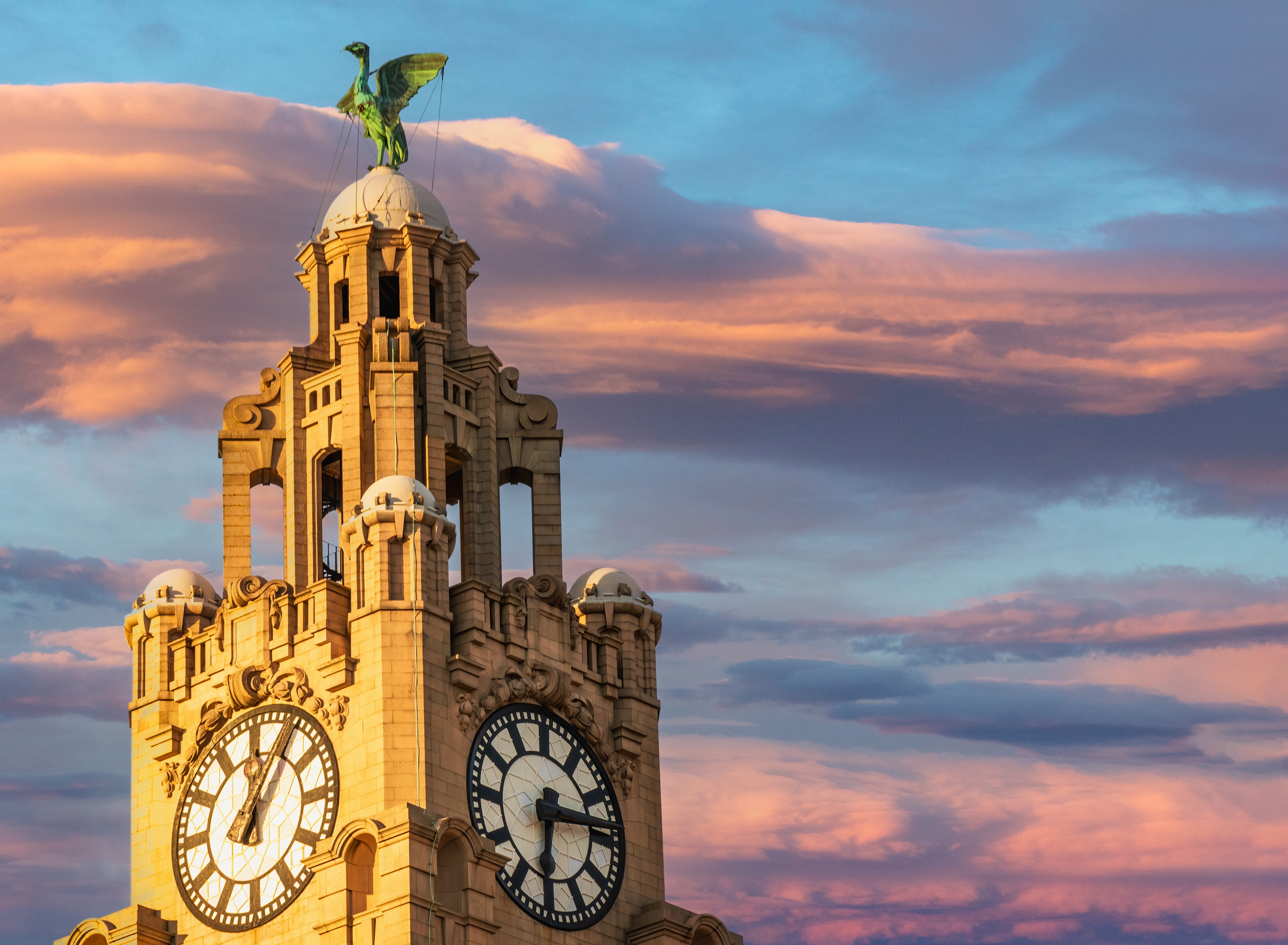 Det ikoniske Royal Liver Building med karakteristiske urtårne og berømte Liver Bird skulpturer badet i gyldent solnedgangslys ved Liverpools historiske havnefront