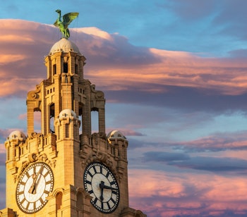 Det ikoniske Royal Liver Building med karakteristiske urtårne og berømte Liver Bird skulpturer badet i gyldent solnedgangslys ved Liverpools historiske havnefront