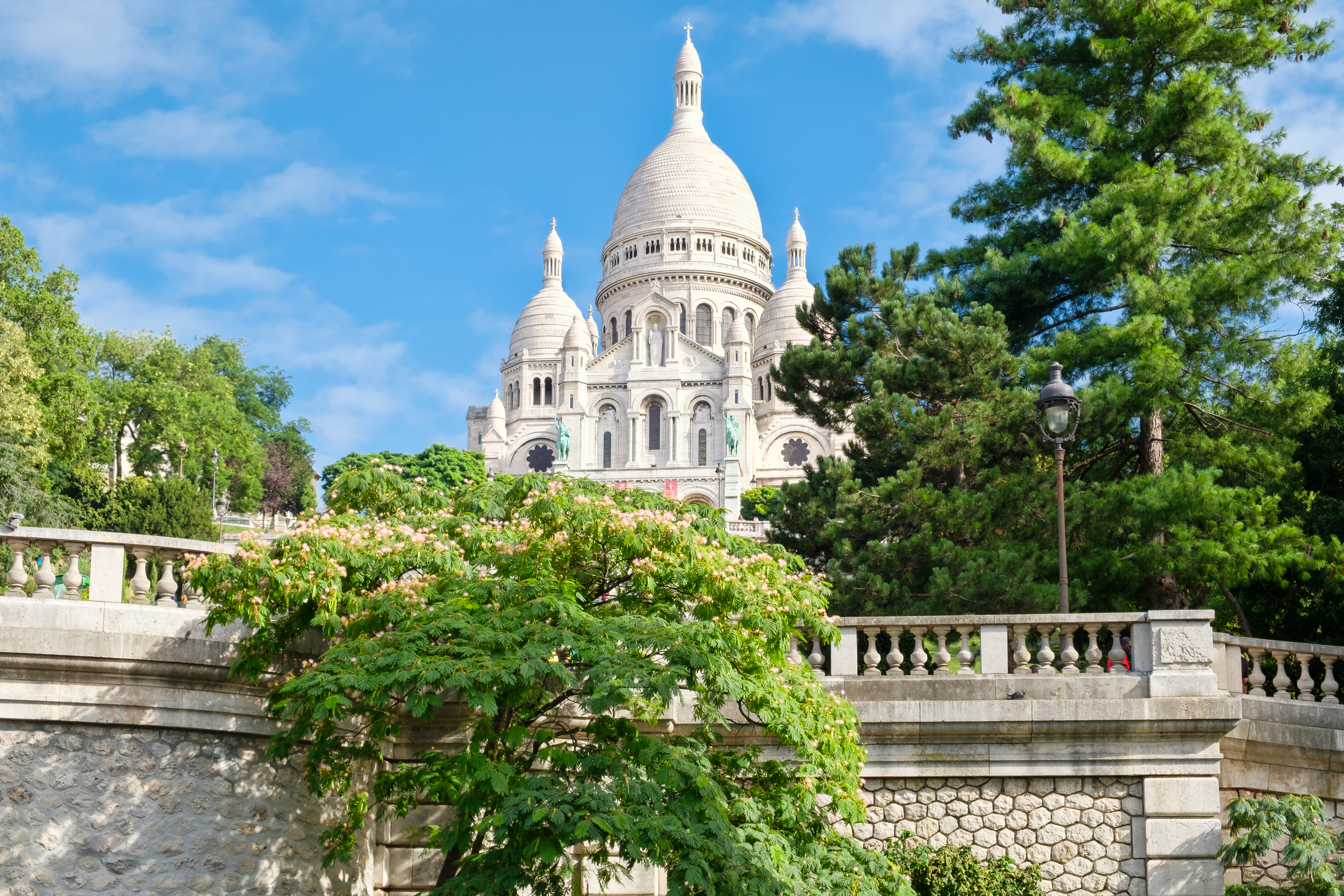Sacré-Cœur Basilika på toppen af Montmartre-bakken i Paris med hvide kupler og grønne træer på en solrig sommerdag