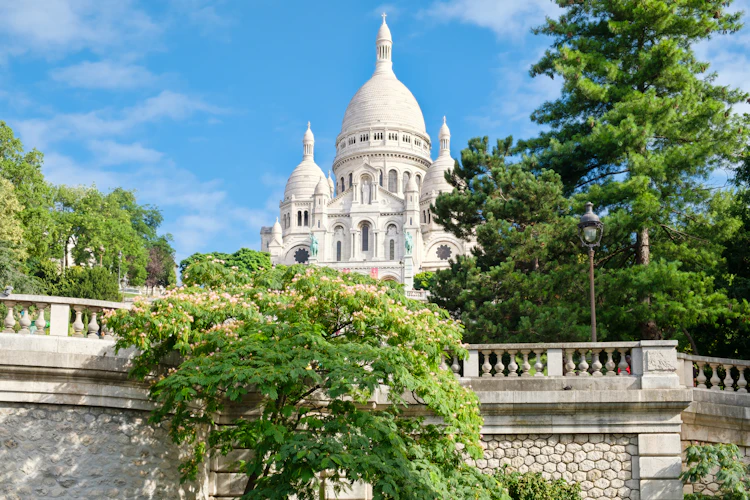 Sacré-Cœur Basilika på toppen af Montmartre-bakken i Paris med hvide kupler og grønne træer på en solrig sommerdag