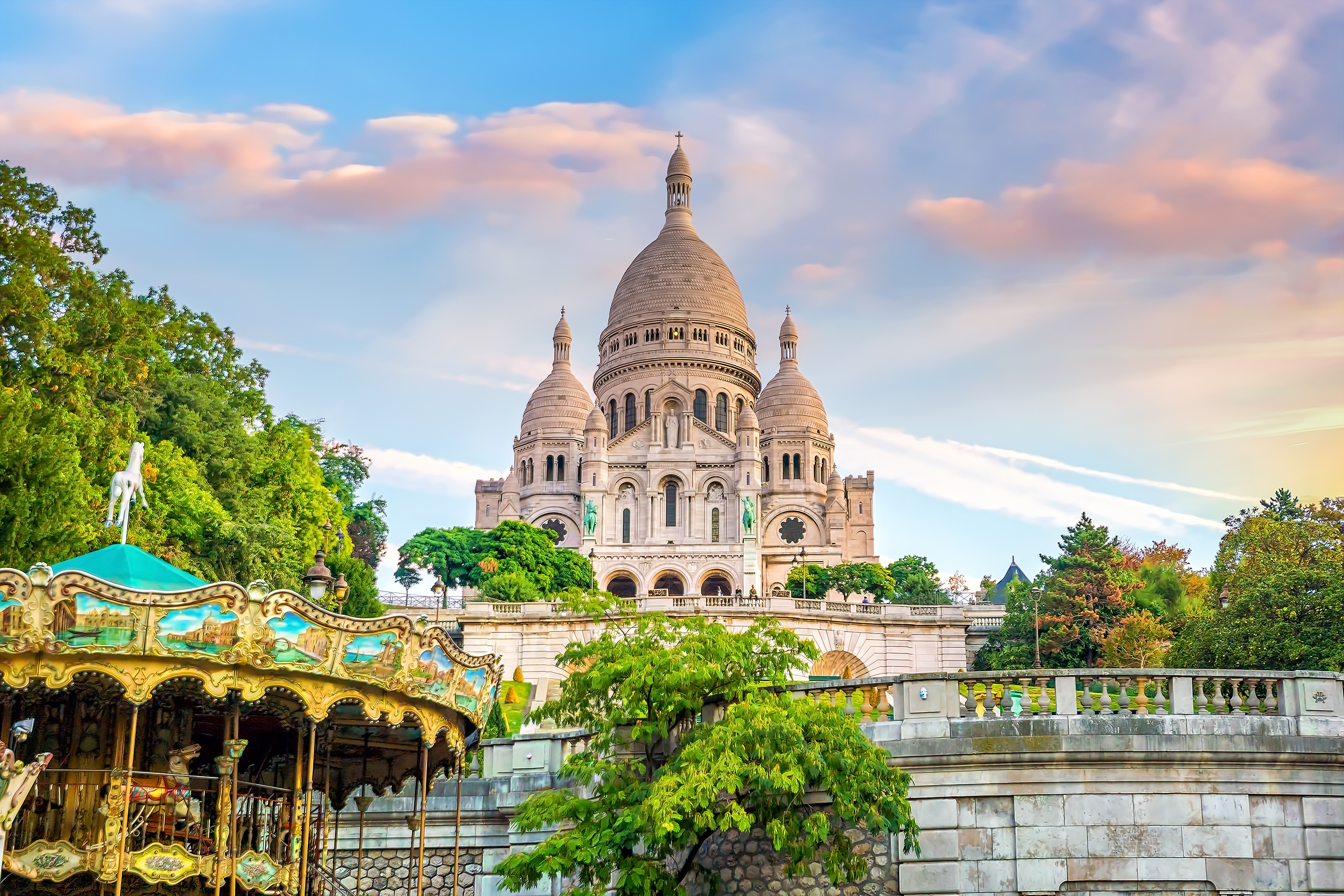 Sacré-Cœur Basilikaen på Montmartre-bakken i Paris med en farverig karrusel i forgrunden og en smuk solnedgangshimmel