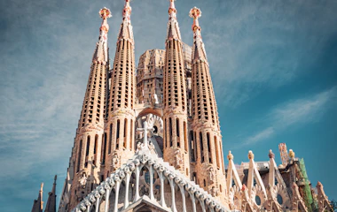 Den ikoniske Sagrada Familia basilika i Barcelona, Spanien, med Antoni Gaudís imponerende spir og detaljerede stenfacade mod en blå himmel