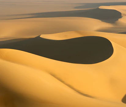 Gyldne sandklitter i Sahara ørkenen med dramatiske skygger og varmt sollys