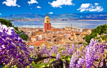 Saint Tropez med historisk kirketårn og terrakottatage med udsigt over Middelhavet på den franske riviera, indrammet af lilla blomster