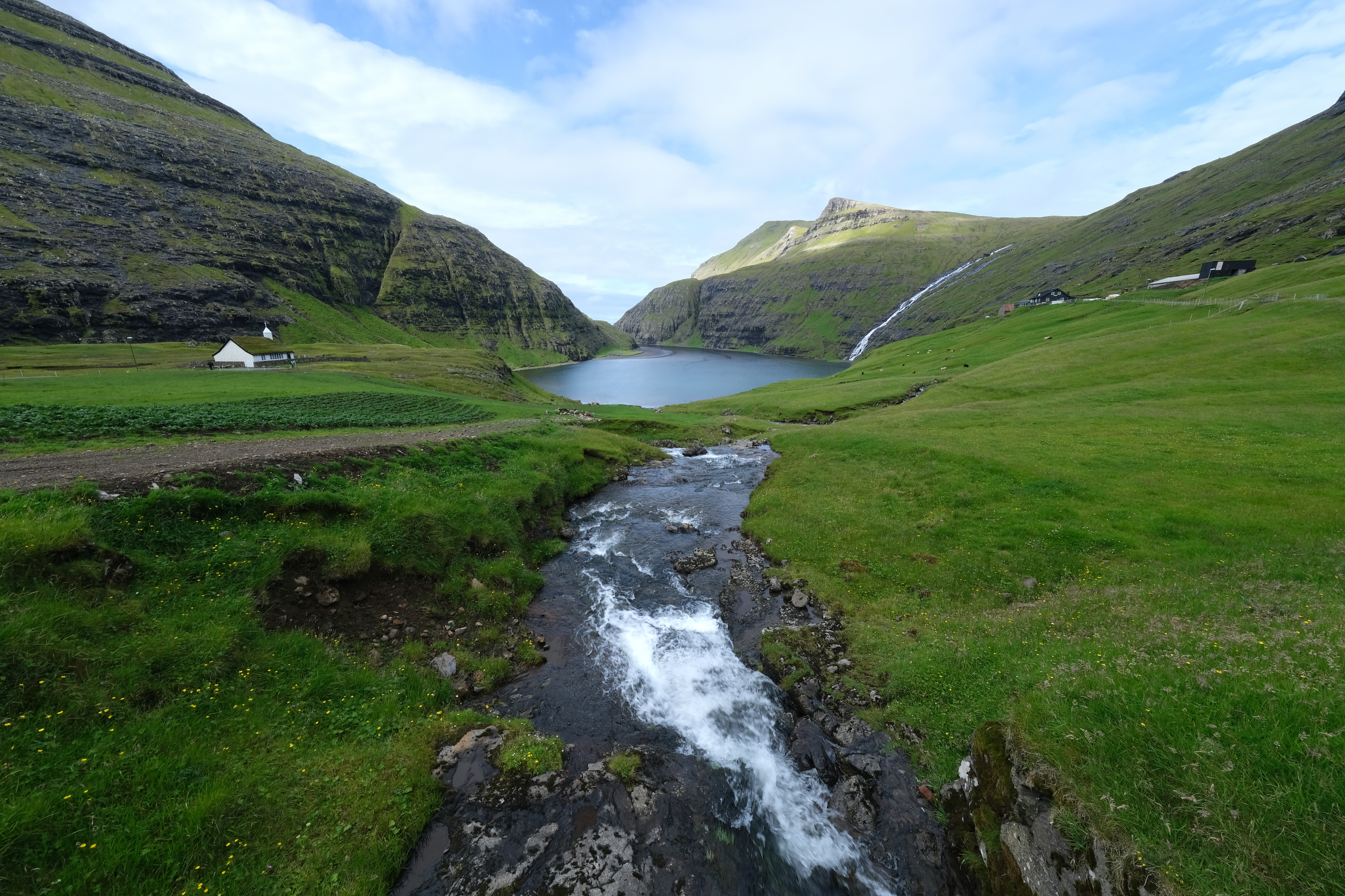 Idyllisk udsigt over Saksun landsby med traditionel kirke omgivet af grønne bjerge og fjorde på Færøerne nær Tórshavn