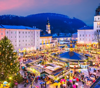 Salzburg julemarked med lysende boder og juletrae i snedaekket torv ved aftentide
