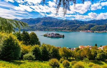 Malerisk solnedgang over San Giulio-øen med farverige bygninger omgivet af Orta-søens blå vand i Piemonte, Italien