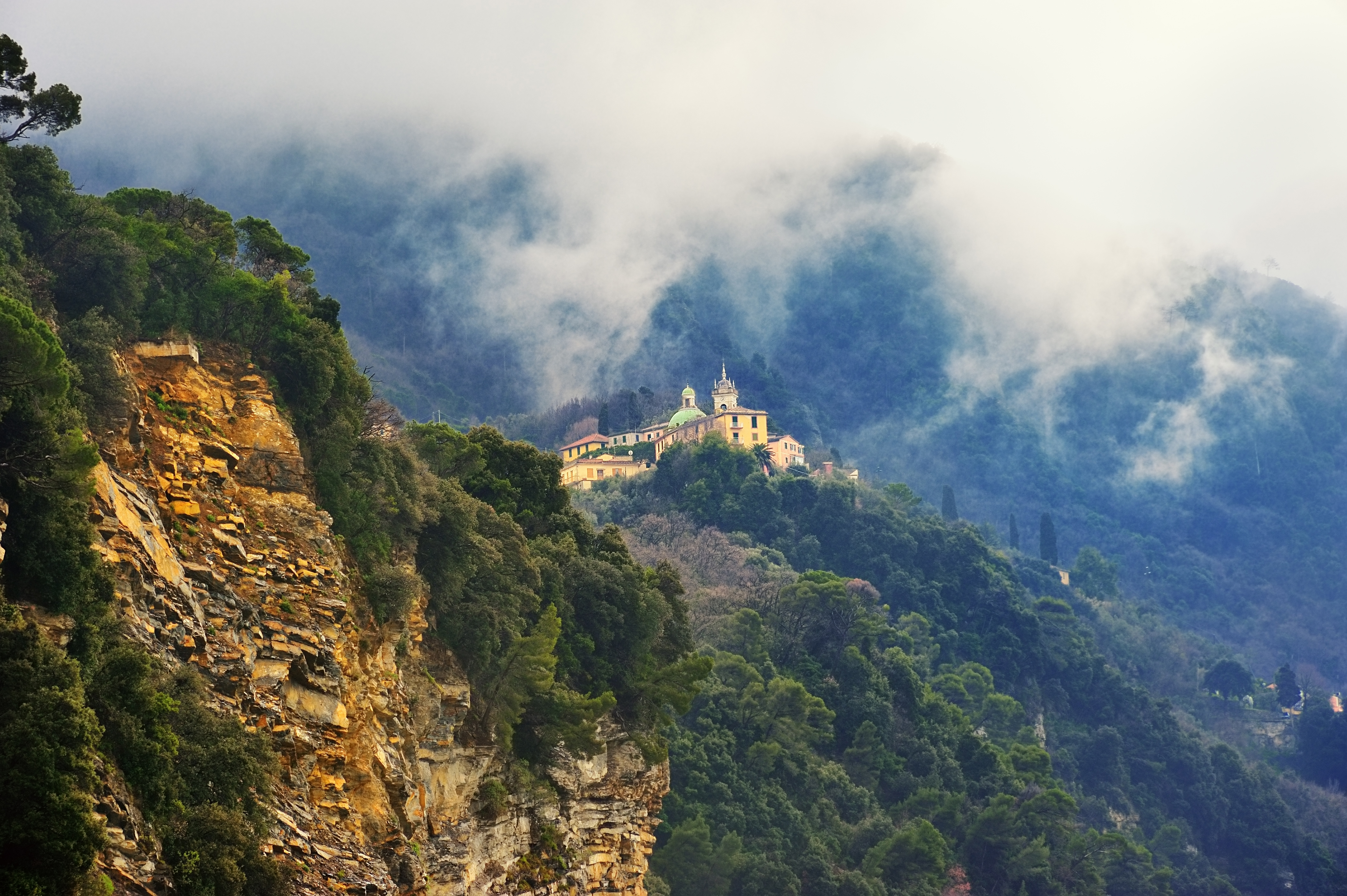 Den historiske San Rocco kirke på en dramatisk klippetop i Camogli ved den italienske riviera, omgivet af frodig grøn skov og bjergdis