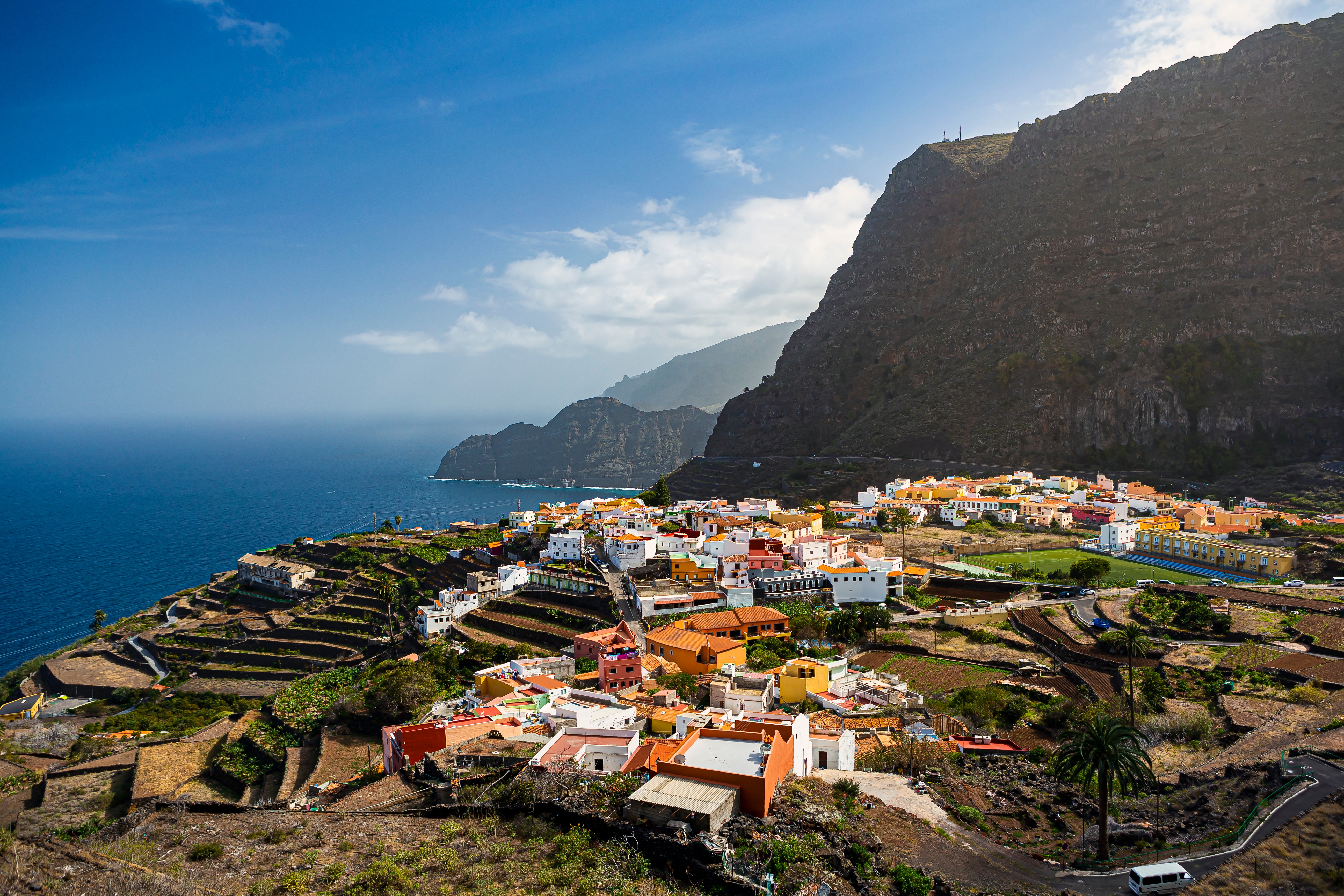 Panoramaudsigt over San Sebastian de la Gomera med farverige bygninger omgivet af terrasserede marker og dramatiske klipper på De Kanariske Øer
