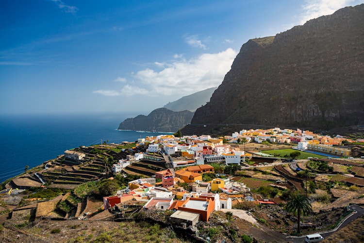 Panoramaudsigt over San Sebastian de la Gomera med farverige bygninger omgivet af terrasserede marker og dramatiske klipper på De Kanariske Øer