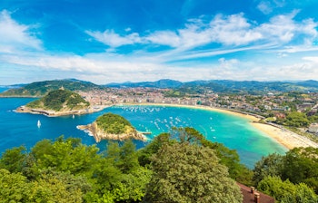 Panoramisk luftfoto af San Sebastian på en smuk sommerdag, der fremhæver byens kystlinje i Spanien.
