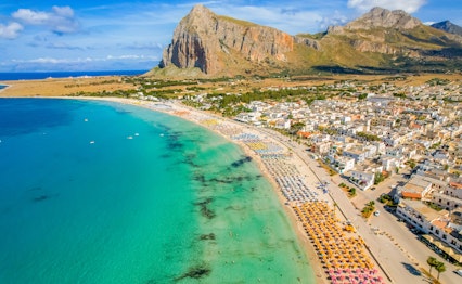 Idyllisk sandstrand ved San Vito lo Capo med Monte Monaco bjerget i baggrunden, krystalklart blåt vand og gyldent sand på Siciliens nordvestlige kyst