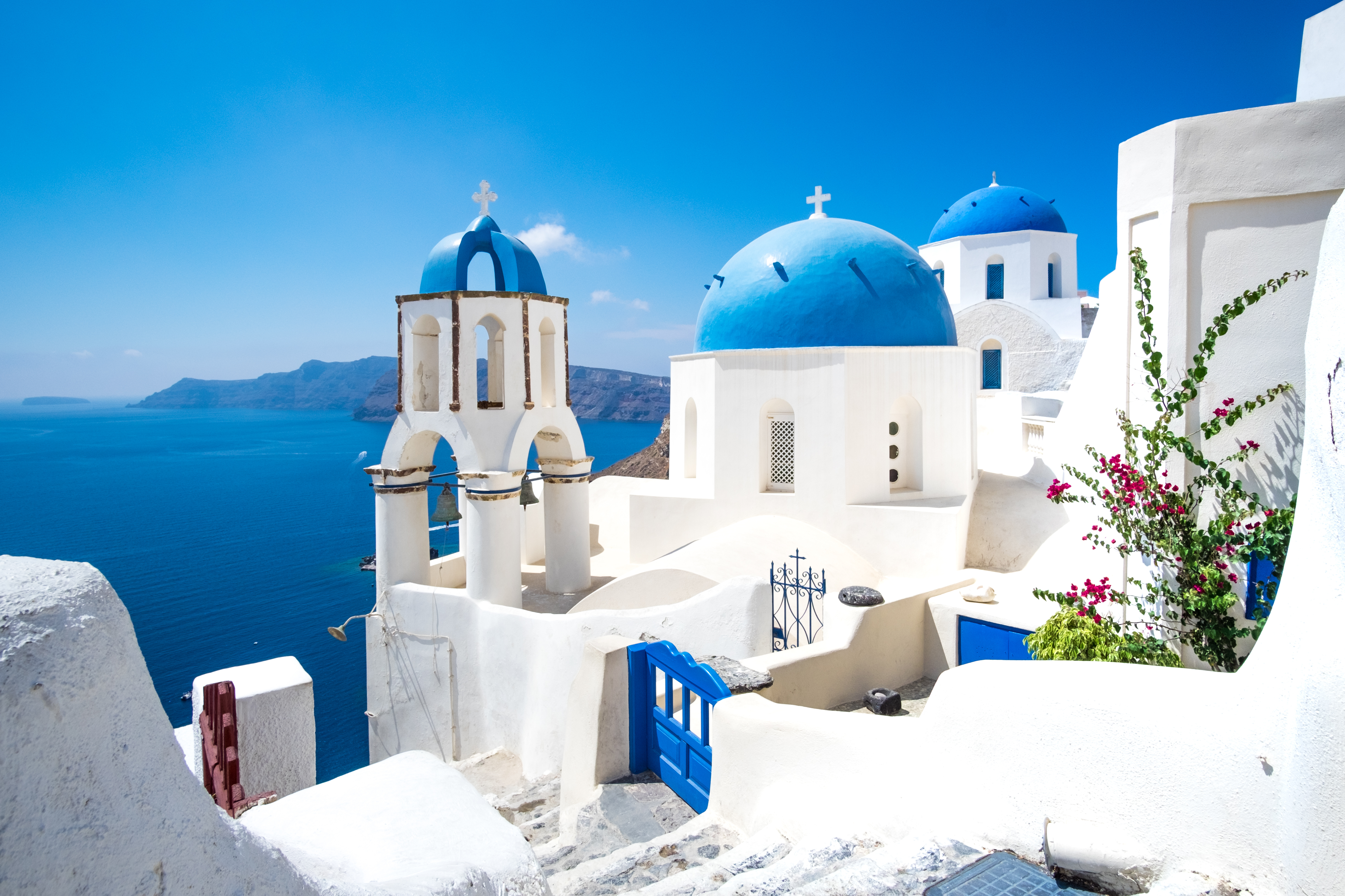 Smuk hvid kirke med blå kupler og udsigt over Ægæerhavet i Santorini