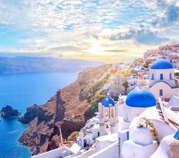 Panoramaudsigt over Oia i Santorini med traditionelle hvide bygninger og blå kupler med udsigt over Ægæerhavets caldera ved solnedgang