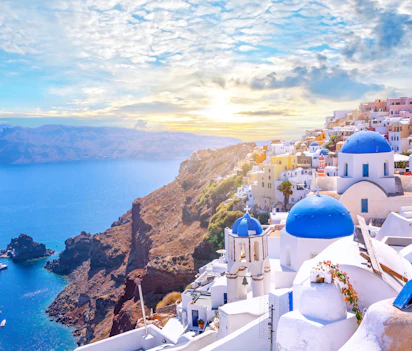 Panoramaudsigt over Oia i Santorini med traditionelle hvide bygninger og blå kupler med udsigt over Ægæerhavets caldera ved solnedgang