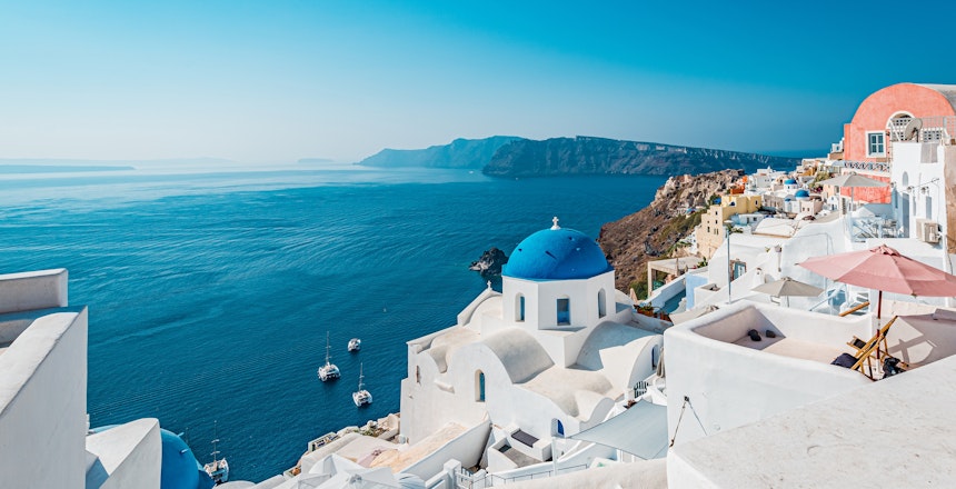 Betagende solnedgangsudsigt over Oia-landsbyen med ikoniske hvide bygninger og blå kupler med udsigt over det Ægæiske Hav på Santorini
