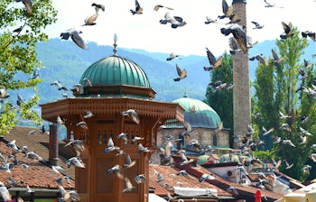 Den historiske Sebilj-fontæne i Sarajevos gamle bydel Bascarsija med flyvende duer og traditionel arkitektur