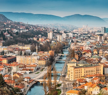 Panoramaudsigt over Sarajevos byskab ved solnedgang med Miljacka-floden der løber gennem den historiske bymidte omgivet af bjerge i Bosnien