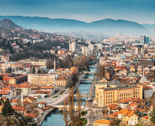 Panoramaudsigt over Sarajevos byskab ved solnedgang med Miljacka-floden der løber gennem den historiske bymidte omgivet af bjerge i Bosnien