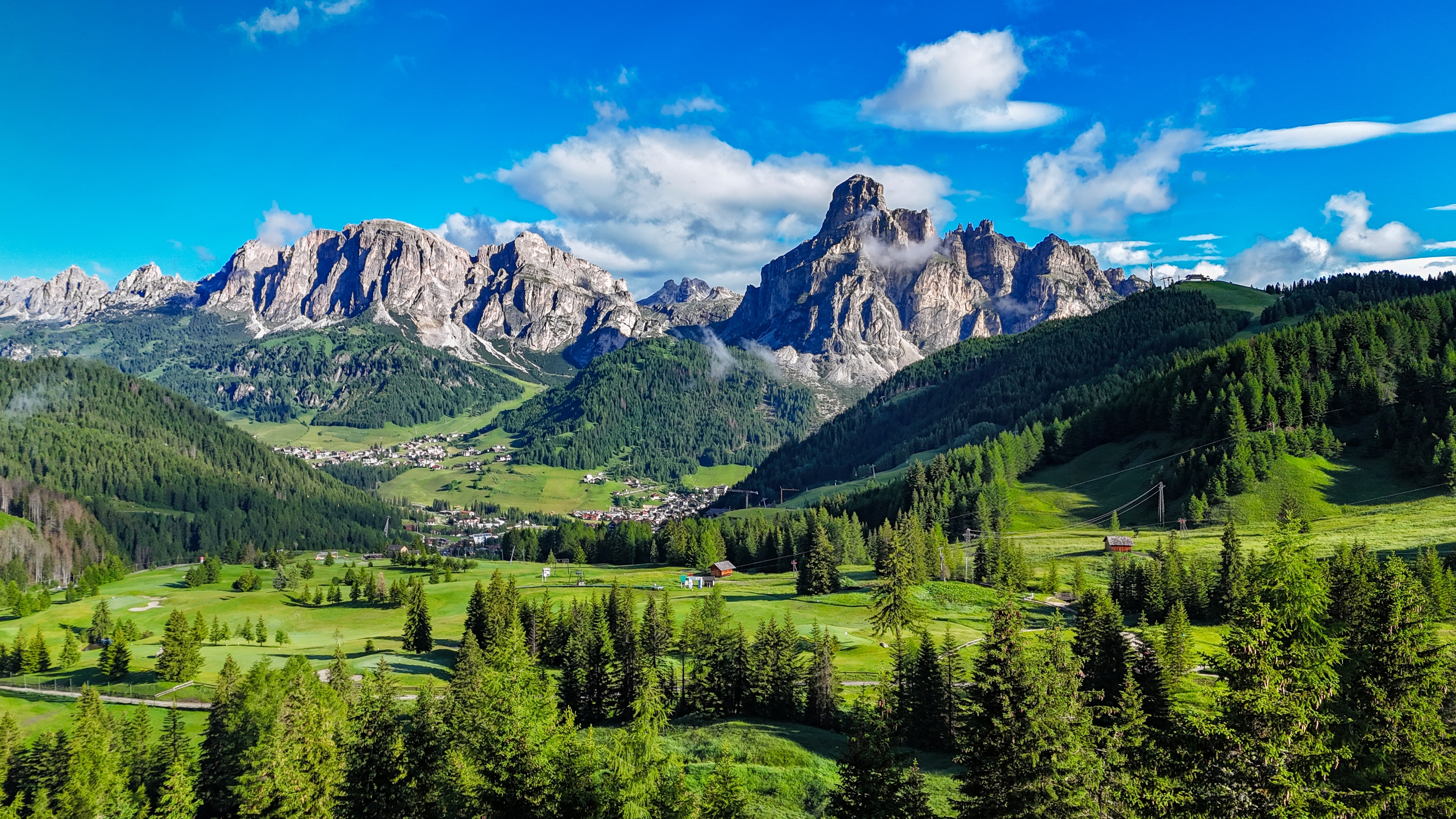 Panoramaudsigt over Sassongher-bjerget og den grønne dal ved Corvara i Alta Badia, Dolomitterne, Italien, med tæt skov og en hyggelig alpelandsby