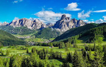 Panoramaudsigt over Sassongher-bjerget og den grønne dal ved Corvara i Alta Badia, Dolomitterne, Italien, med tæt skov og en hyggelig alpelandsby