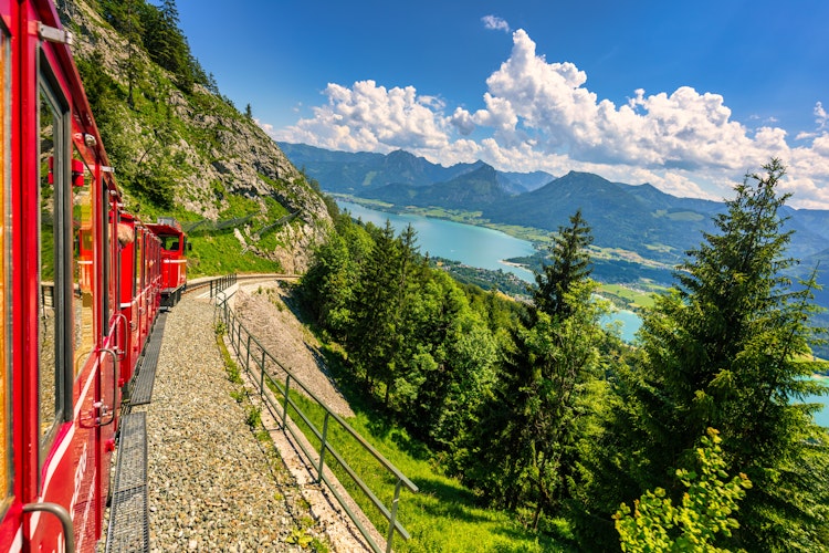 Den ikoniske røde Schafbergbahn bjergbane kører gennem grønne alpelandskaber i Salzburg-regionen med udsigt over Wolfgangsee søen i Østrig