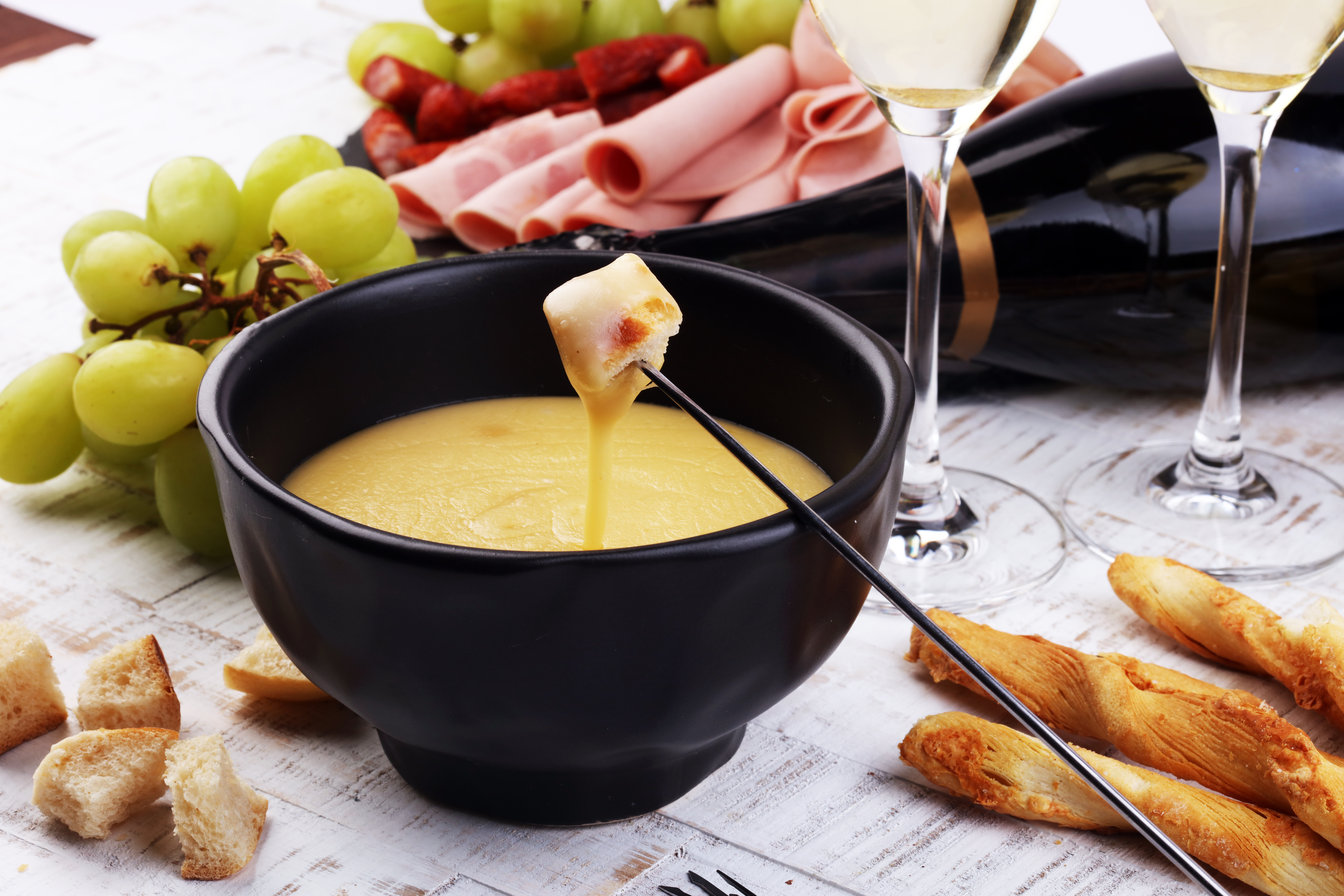 Traditionel schweizisk ostefondue med brød, charcuteri, druer og hvidvin serveret på en hyggelig vinteraften i en alperestaurant