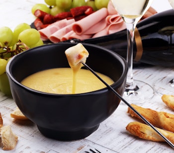 Traditionel schweizisk ostefondue med brød, charcuteri, druer og hvidvin serveret på en hyggelig vinteraften i en alperestaurant