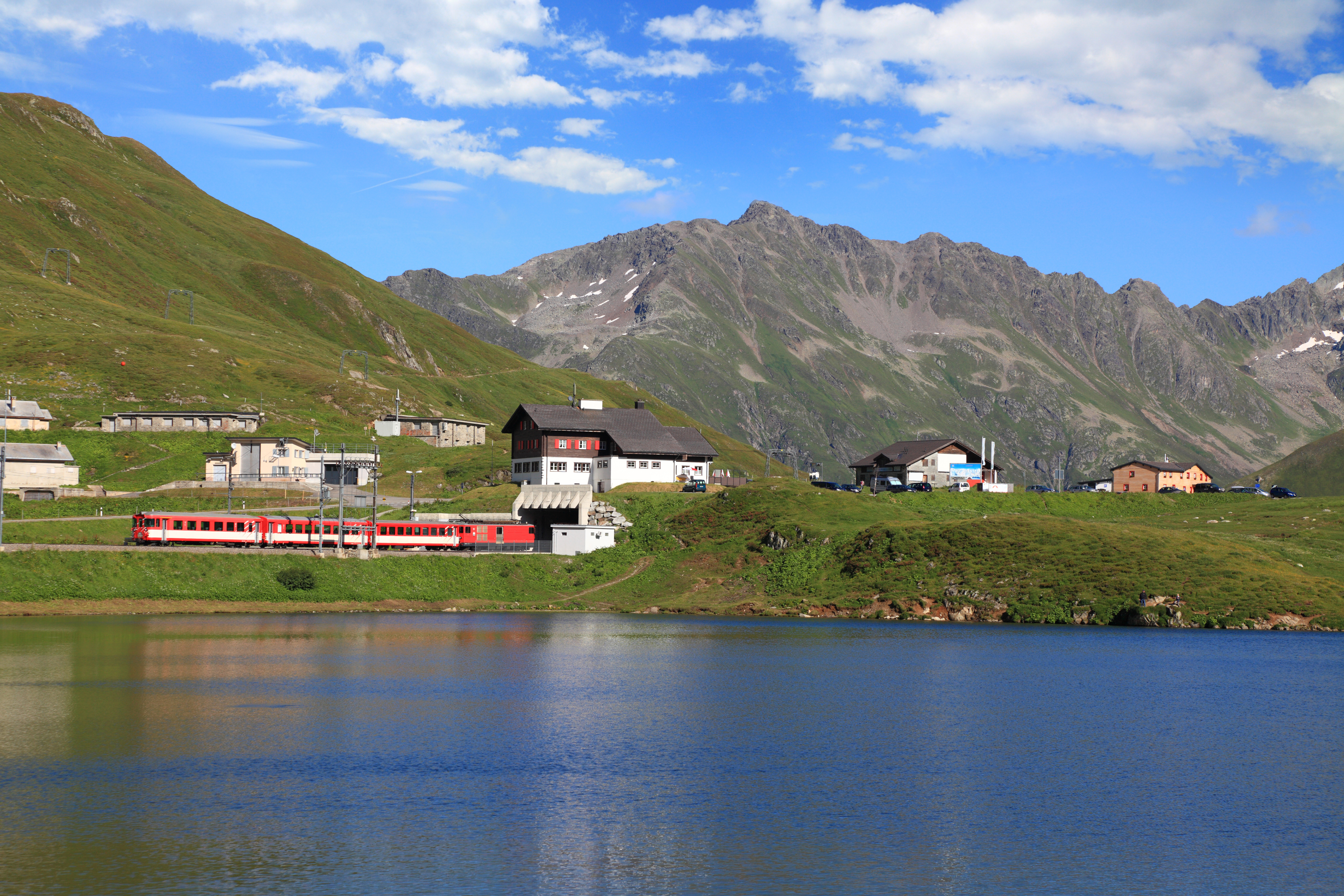 Rødt schweizisk bjergtog kører gennem alpelandskab med sø og snedækkede bjerge