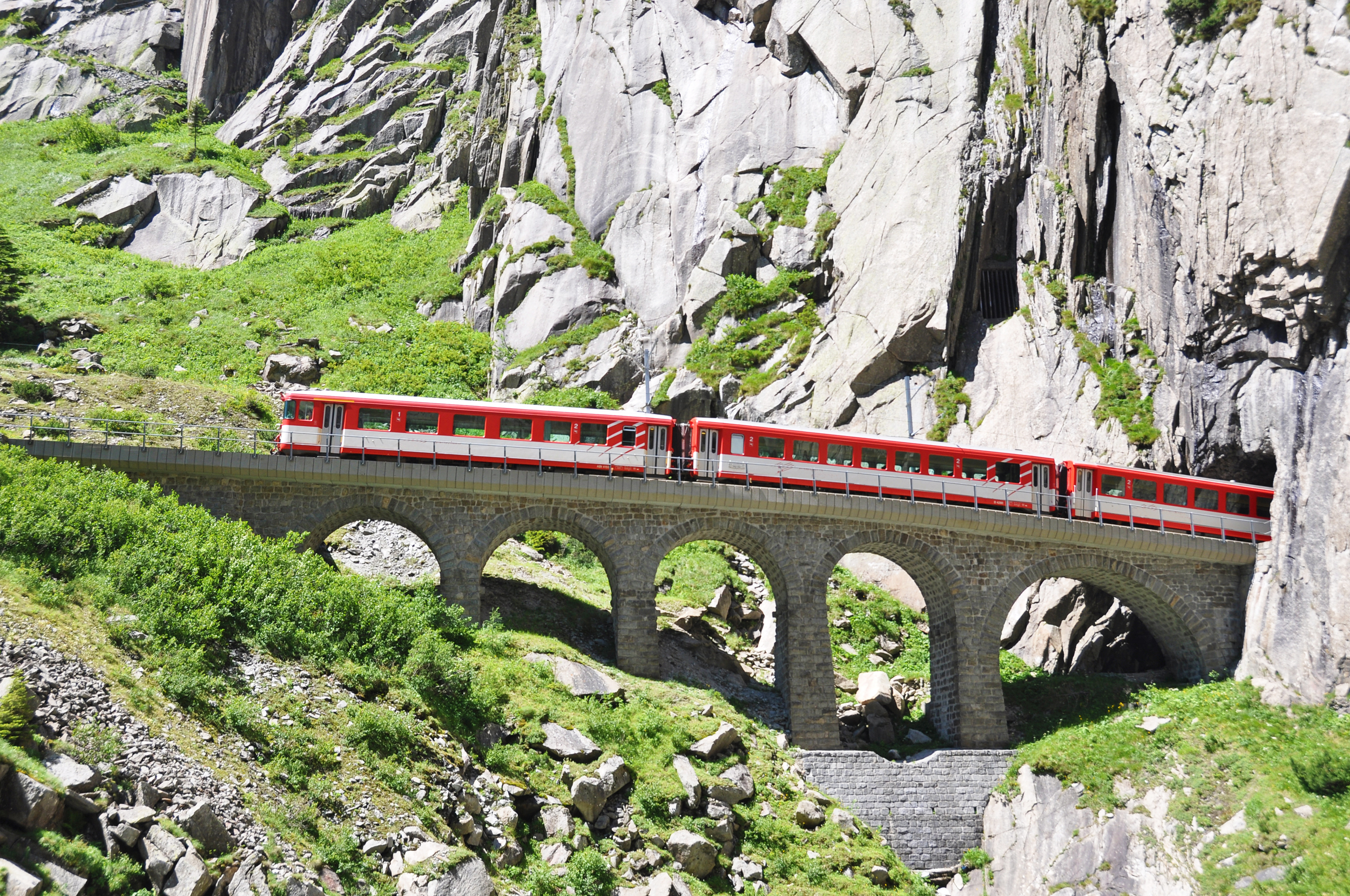 Rødt schweizisk bjergtog krydser historisk stenviadukt gennem dramatisk alpelandskab i Schweiz