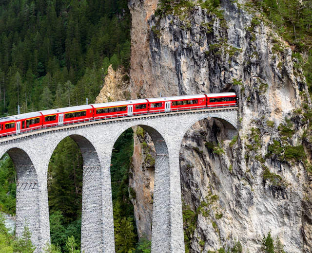 Rødt schweizisk tog kører over den berømte Landwasser Viadukt i de schweiziske alper